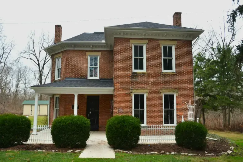 Two-story red-brick house with a white porch and boxwoods