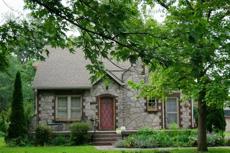 Stone cottage with a steep roof under tall trees