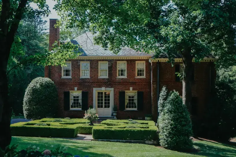 Two-story Georgian brick house behind clipped hedges